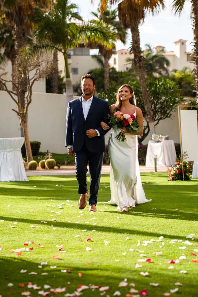 Bride walking down the aisle at Secrets Puerto Los Cabos, capturing an elegant destination wedding moment with beautiful ocean views and a romantic beachside setting.