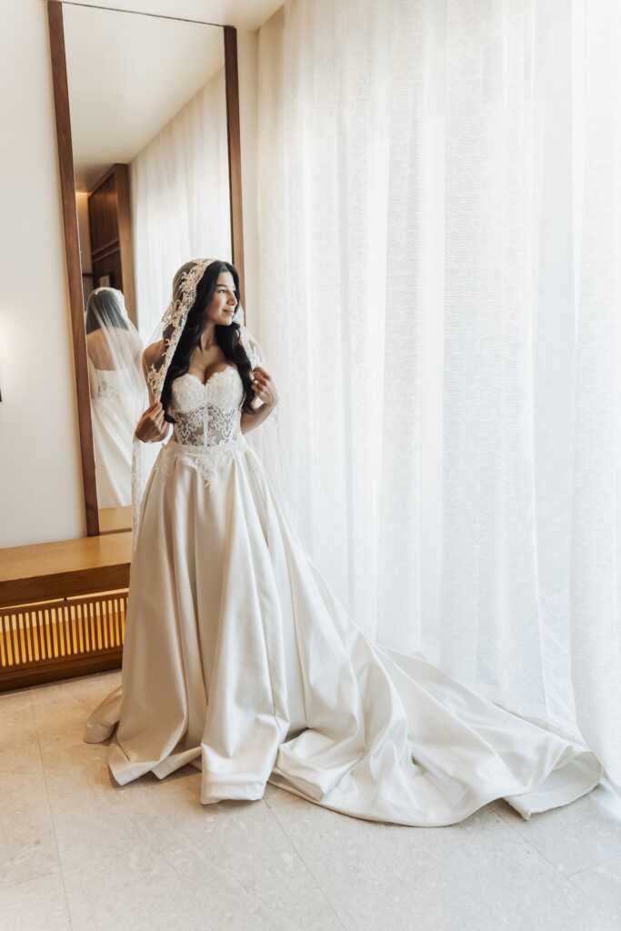 Bride standing by a large window in her room at Nobu Hotel Los Cabos, ready for her destination wedding.